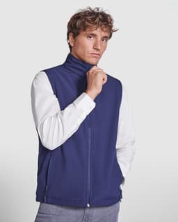 A navy softshell vest with a high collar, featuring a zip front and side pockets, worn by a model.
