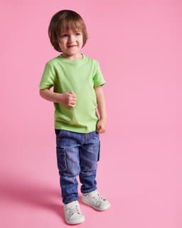A young child wearing a light green t-shirt and blue jeans, standing against a pink background.