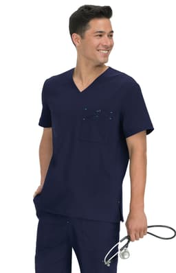 A man wearing a navy scrub top with a pocket, holding a stethoscope, smiling at the camera.