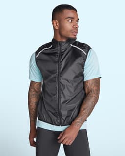 A man wearing a black ultra-light windbreaker vest over a light blue shirt, featuring reflective details and a logo.