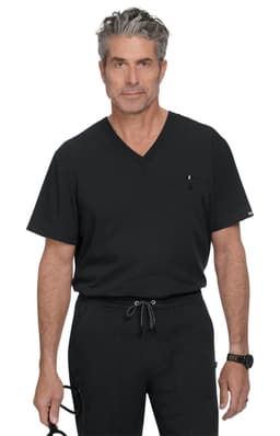 A man in a black V-neck scrub top stands confidently, wearing black trousers and holding glasses. The outfit features a pocket and branding.