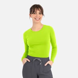 A woman is wearing a bright lime green long-sleeve tee paired with grey pants. The tee features a logo.