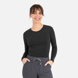A fitted black long-sleeve underscrub tee worn by a model, paired with grey pants. The product features a logo.