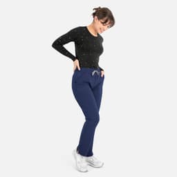 A woman in a black long-sleeve top and navy blue pants, smiling while standing with her hands in her pockets.