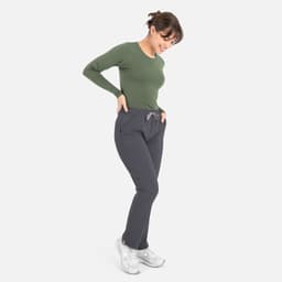 A model in a green long-sleeve underscrub tee and grey pants, featuring a branded logo on the tee.