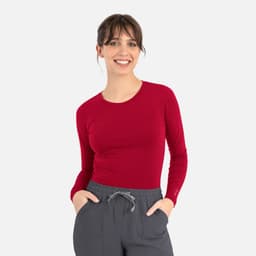 A fitted long-sleeve underscrub tee in red, worn with grey pants, featuring a logo on the sleeve.