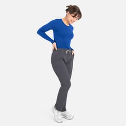 A woman is wearing a blue long-sleeve underscrub tee paired with grey pants and white shoes.