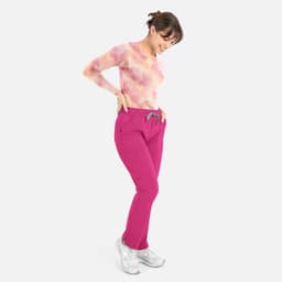 A woman wearing a tie-dye pink and orange long-sleeve tee with pink pants, posed smiling downwards.