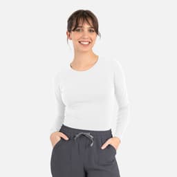 A white long-sleeve underscrub tee, paired with grey pants, displayed on a smiling model.