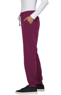 A pair of burgundy jogger pants with pockets and a drawstring waist, styled with a white long-sleeve top and black shoes.