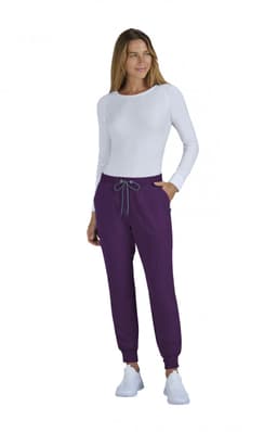A woman wearing a fitted white long-sleeve top and purple jogger pants, with a drawstring at the waist.