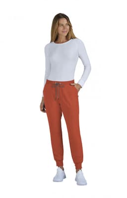 A woman wearing orange jogger pants and a long-sleeve white top, featuring a brand logo.