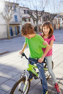 A boy in a green T-shirt rides a bike while a girl in a pink T-shirt smiles behind him.