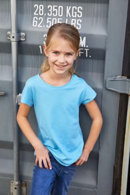 A girl wearing a light blue T-shirt and jeans, posing in front of a container. The shirt has a logo.