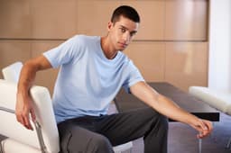 A light blue men's t-shirt displayed on a seated model, featuring a relaxed fit and a simple design.