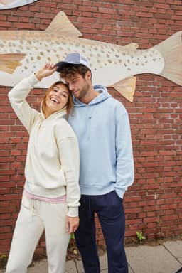 A cream and blue hoodie worn by a man and woman, smiling in front of a brick wall with a fish mural.