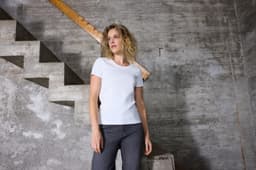 A white ladies T-shirt with a fitted design, displayed against a textured concrete wall and staircase.