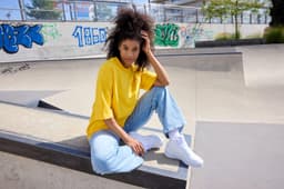 A yellow oversized T-shirt paired with light blue jeans, worn by a person sitting at a skate park.