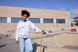 An oversized hooded jacket in white, worn by a person standing at a skatepark with graffiti.