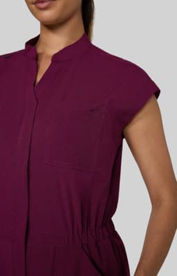 A close-up of a maroon jumpsuit featuring short sleeves and a collared neckline. It has a pocket detail and an elastic waistband.