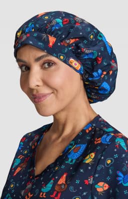 A navy bouffant scrub cap featuring colourful patterns of animals and celestial designs, worn by a smiling woman.