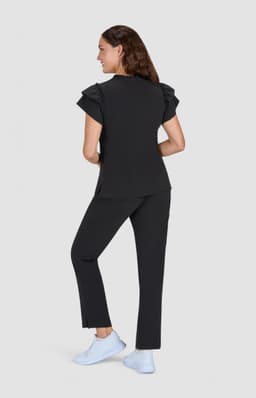 A black top with ruffle sleeves paired with black pants, modelled from the back, featuring light blue footwear.