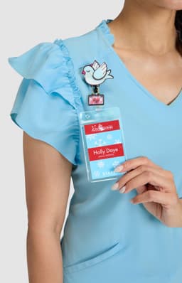 A blue top with ruffled sleeves, featuring a badge holder with a decorative clip and a bird design.