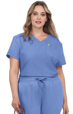 A woman wearing a light blue scrub top with a pocket and short sleeves, featuring a small logo.