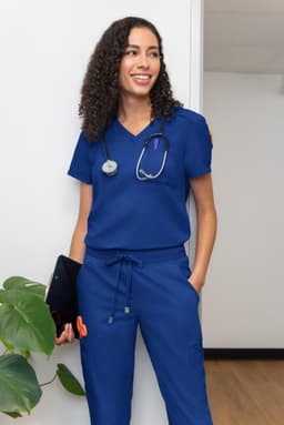 A woman wearing a blue medical scrub set with a stethoscope around her neck, standing in an indoor setting.