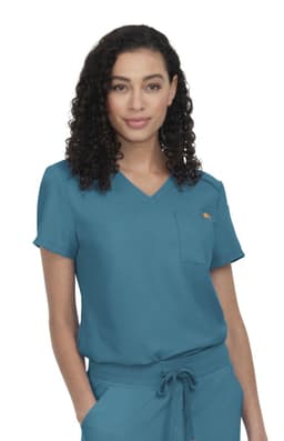 A teal scrub top featuring short sleeves and a pocket, worn by a model with curly hair.