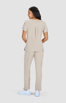 A woman wearing a beige top and matching trousers, facing away from the camera, showcasing a simple design.