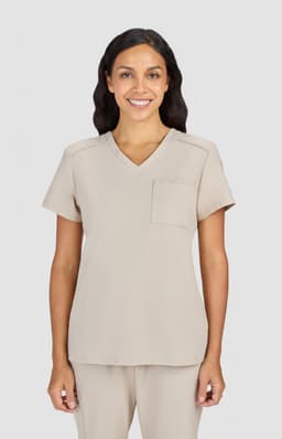 A scrub top in a light beige colour, featuring a V-neck and a single chest pocket. It has branding on the sleeve.