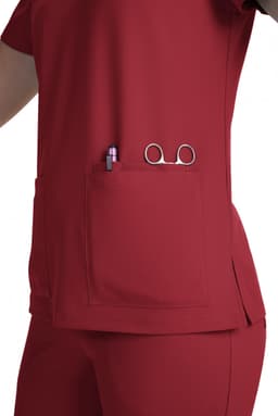 A red scrub top featuring a large pocket containing a pen and scissors, with a simple design and no visible logos.