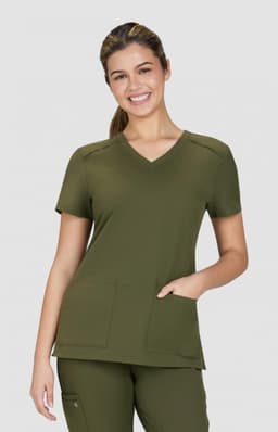 A scrub top in olive green with a V-neck design and two front pockets, modelled by a smiling woman.