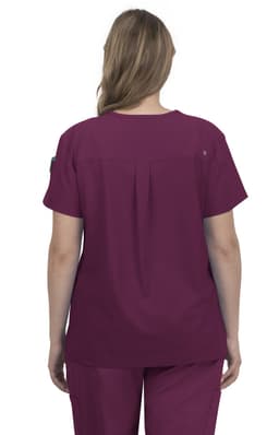 A back view of a woman wearing a burgundy scrub top. The top features a pleat detail and a logo on the sleeve.