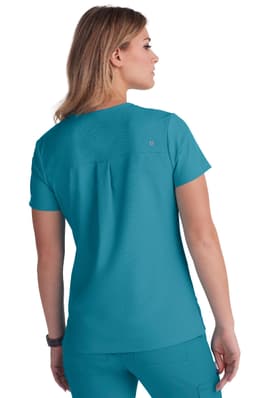A teal women's top with short sleeves and a back pleat, featuring a brand logo.