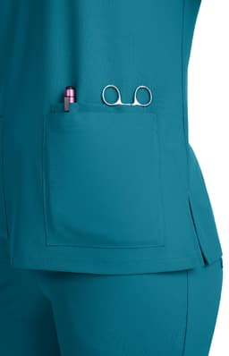 A teal scrub top featuring a pocket with a pen and scissors visible, alongside a branded logo.