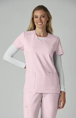 A healthcare top in pink, featuring a v-neck and two front pockets, worn by a smiling model.