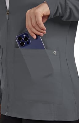 A grey women's jacket featuring a pocket, with a hand placing a phone inside. The jacket has a logo on it.