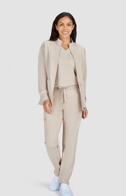 A woman is wearing a beige jacket and matching pants, paired with a simple top and white shoes. The outfit is stylish and modern.