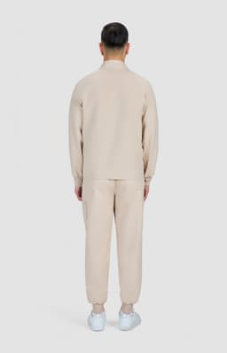 A beige men's jacket and matching pants are displayed from the back, featuring a simple design and a logo.