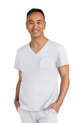 A man wearing a light grey scrub top with a V-neck and a pocket on the chest, smiling towards the camera.
