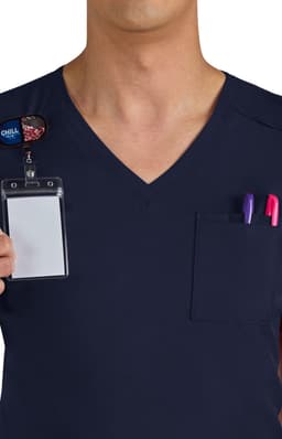 A navy scrub top featuring a chest pocket with pens and an ID badge holder. It has a logo on the badge.
