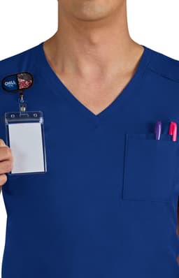 A navy blue scrubs top featuring a breast pocket with pens and a badge holder. The wearer is partially visible.