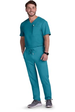 A man in teal scrubs stands smiling, wearing grey shoes and a watch. The outfit includes a top with a pocket and drawstring pants.