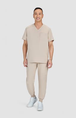A man wearing a beige medical scrub set consisting of a V-neck top and jogger-style pants, paired with white shoes.