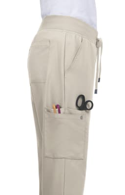 A beige Atria Pant featuring side pockets, one with scissors and pens, and a drawstring waist.