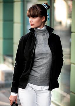 A black women's jacket is worn over a grey sweater, paired with white trousers, featuring a collar and a zip.