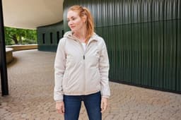 A light beige ladies bomber jacket with a hood, showcased on a woman standing in an outdoor setting.