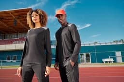 A long-sleeve men's running shirt in black, worn by a model on a track, featuring a logo.